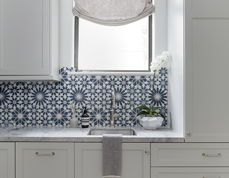 Laundry room with custom wood cabinets, marble countertop with brass sink fixture and classic blue and white geometric tile backsplash Houston, TX